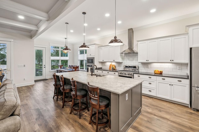kitchen with a sink, light wood-style floors, wall chimney exhaust hood, crown molding, and appliances with stainless steel finishes