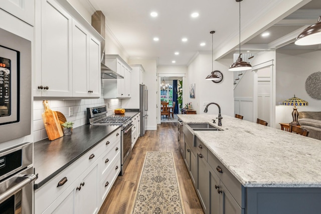 kitchen featuring stainless steel appliances, a sink, a spacious island, decorative backsplash, and wood finished floors