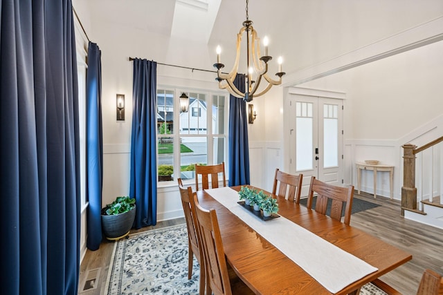 dining room featuring wainscoting, a decorative wall, light wood finished floors, and an inviting chandelier