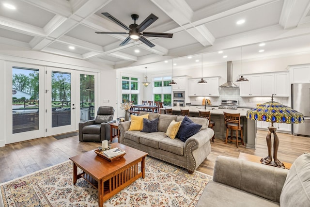 living area with light wood-style flooring, beam ceiling, a ceiling fan, and coffered ceiling