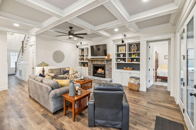 living room with coffered ceiling, wood finished floors, a stone fireplace, beam ceiling, and ceiling fan