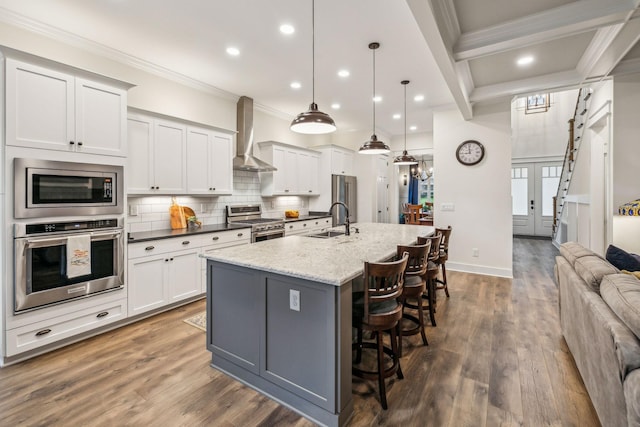 kitchen featuring a sink, wall chimney exhaust hood, crown molding, appliances with stainless steel finishes, and open floor plan