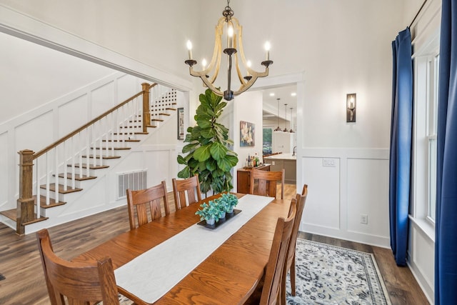 dining space with stairway, a decorative wall, wood finished floors, an inviting chandelier, and visible vents