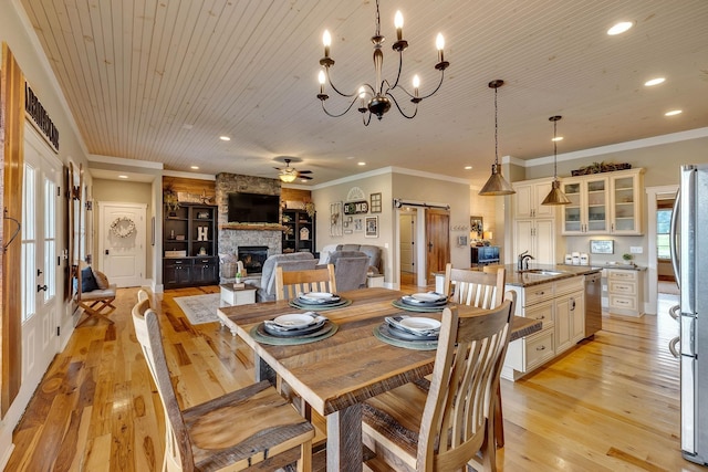 dining room with a barn door, a stone fireplace, ceiling fan with notable chandelier, light wood-style floors, and wooden ceiling