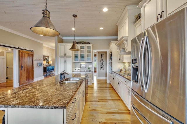 kitchen featuring light wood finished floors, a kitchen island with sink, a sink, a barn door, and appliances with stainless steel finishes