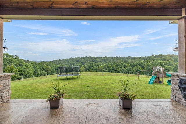 view of patio / terrace with fence, a playground, a wooded view, and a trampoline