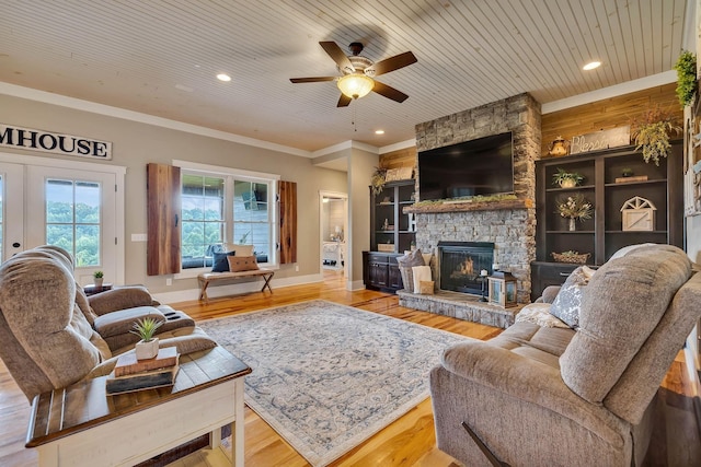 living area with wood finished floors, a ceiling fan, a stone fireplace, and crown molding