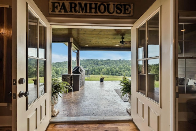 doorway to outside featuring ceiling fan, a wealth of natural light, wood finished floors, and a wooded view