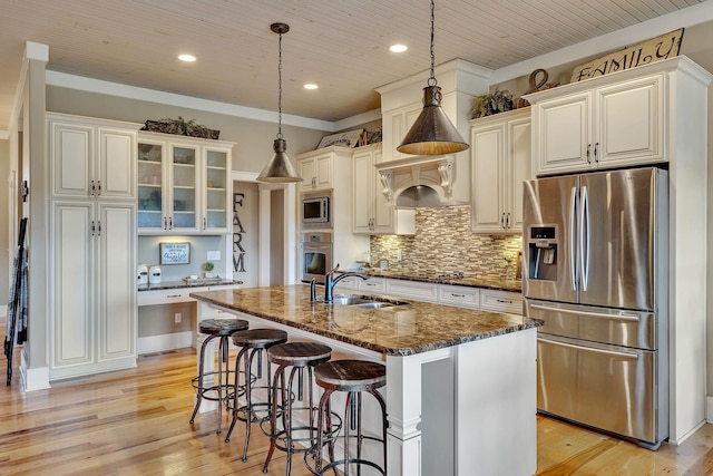 kitchen featuring light wood-style flooring, dark stone countertops, stainless steel appliances, and a sink
