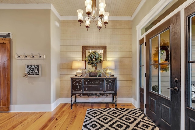 entrance foyer with wood walls, wood finished floors, ornamental molding, baseboards, and a chandelier