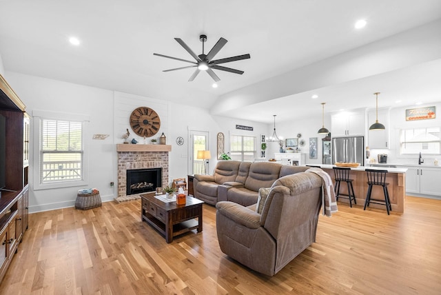 living area featuring a ceiling fan, a fireplace, light wood-style floors, and a healthy amount of sunlight