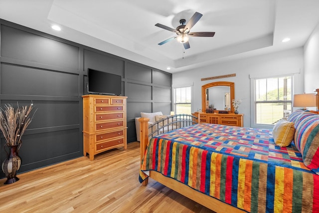 bedroom with a raised ceiling, a decorative wall, light wood-style floors, and recessed lighting