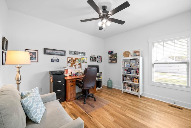 home office with light wood-style floors, visible vents, a ceiling fan, and baseboards