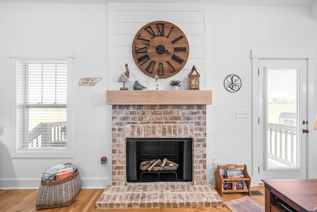 living room featuring baseboards, a brick fireplace, and wood finished floors