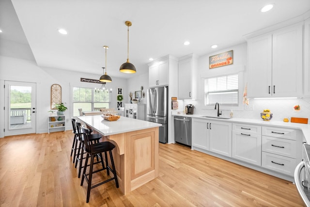 kitchen with light wood finished floors, stainless steel appliances, light countertops, a sink, and a kitchen island