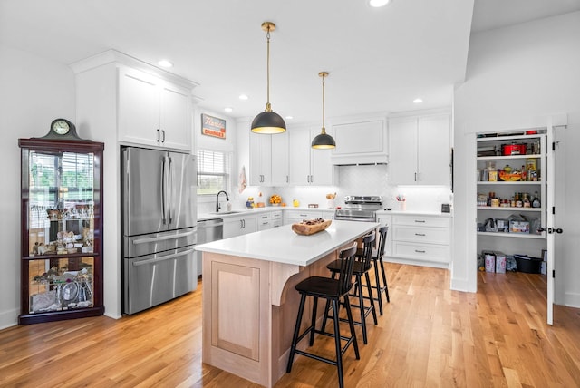 kitchen with light wood finished floors, a kitchen breakfast bar, a sink, light countertops, and appliances with stainless steel finishes
