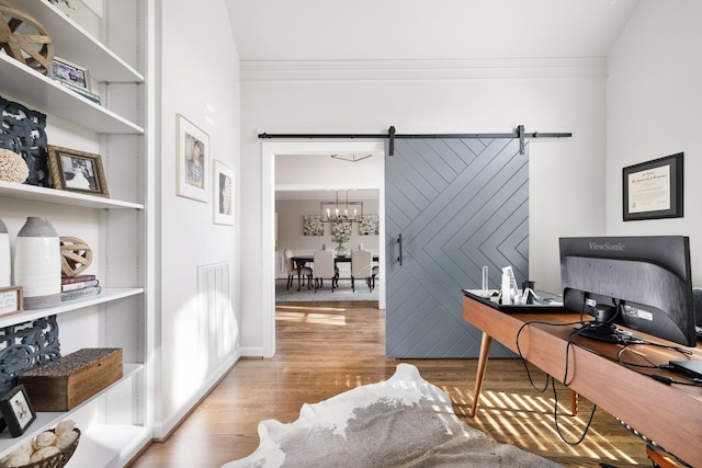 office featuring a barn door, an inviting chandelier, crown molding, and wood finished floors