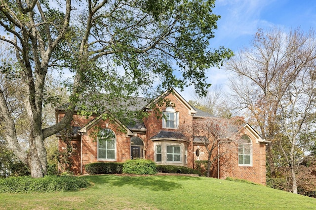 traditional-style house with a shingled roof, a front lawn, and brick siding