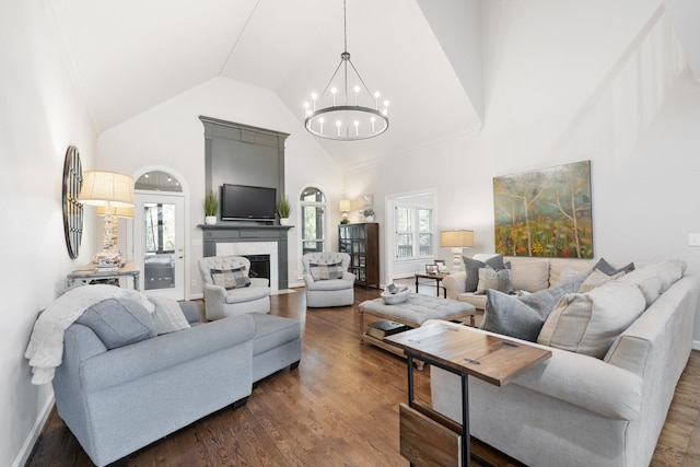 living area with a fireplace with flush hearth, baseboards, a notable chandelier, high vaulted ceiling, and dark wood-type flooring