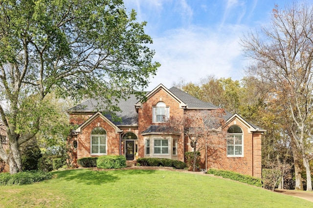traditional home featuring a front lawn, brick siding, and roof with shingles