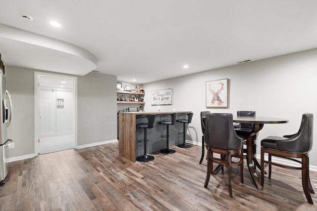 dining room featuring wood finished floors, a bar, and baseboards