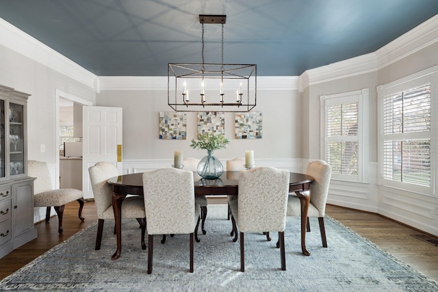 dining space with an inviting chandelier, ornamental molding, a wainscoted wall, and dark wood-style floors