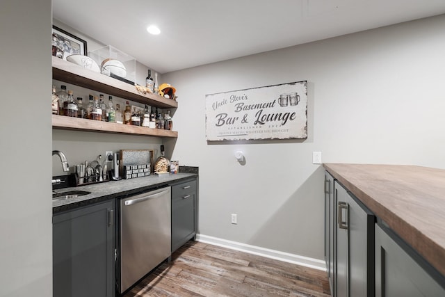 bar with dishwasher, wood finished floors, a sink, baseboards, and indoor wet bar