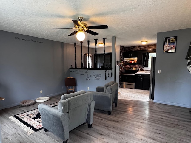 living room with a textured ceiling, ceiling fan, light wood-style flooring, and baseboards