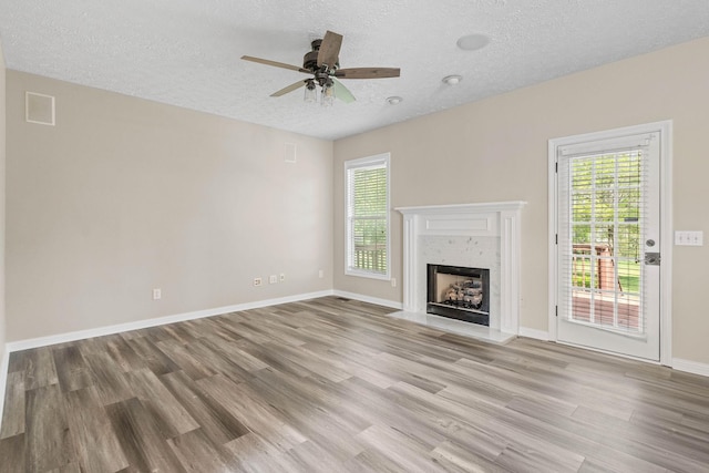 unfurnished living room featuring light wood-style floors, visible vents, a ceiling fan, a textured ceiling, and a fireplace with flush hearth