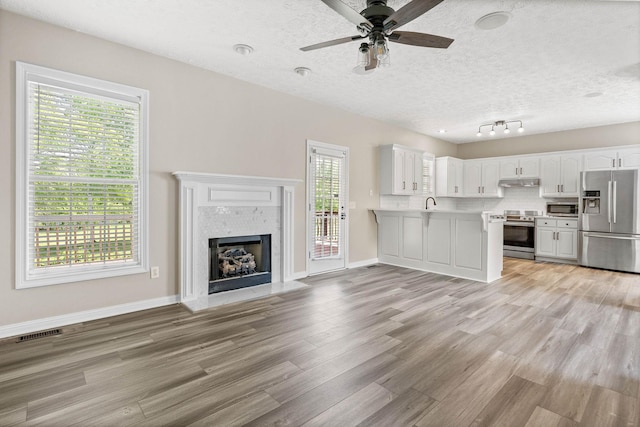 unfurnished living room featuring visible vents, ceiling fan, baseboards, light wood-type flooring, and a fireplace