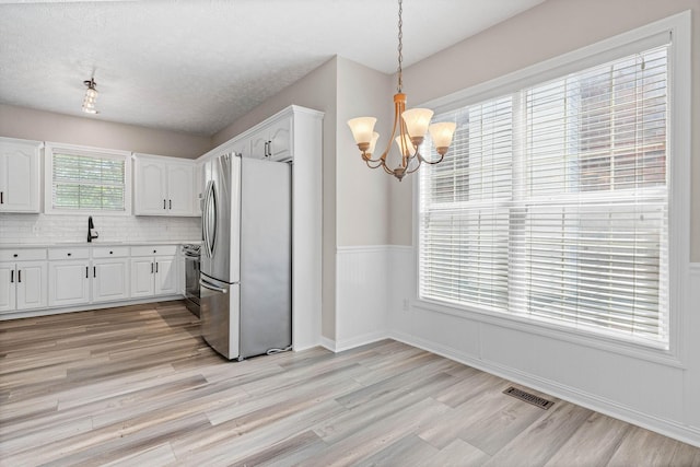 kitchen with freestanding refrigerator, a chandelier, light wood finished floors, white cabinetry, and visible vents