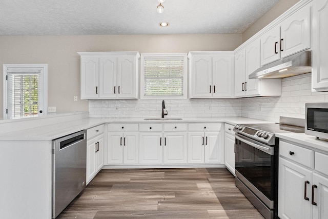 kitchen featuring appliances with stainless steel finishes, under cabinet range hood, white cabinets, a sink, and a peninsula