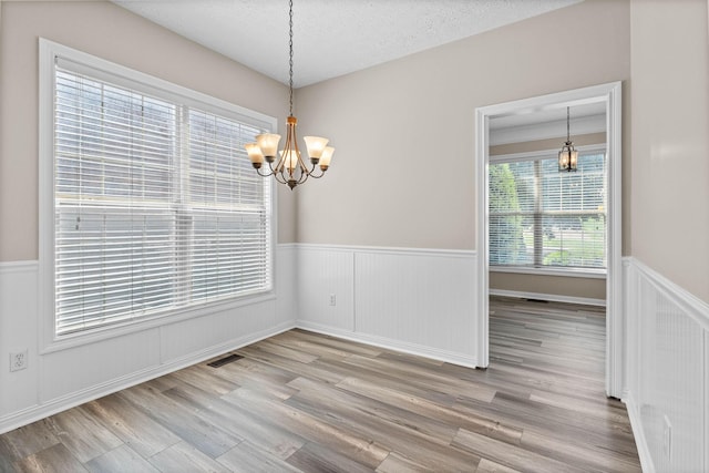 unfurnished dining area with wood finished floors, an inviting chandelier, wainscoting, visible vents, and a textured ceiling
