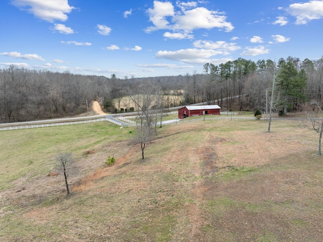 view of yard featuring a wooded view, fence, an outbuilding, and a rural view