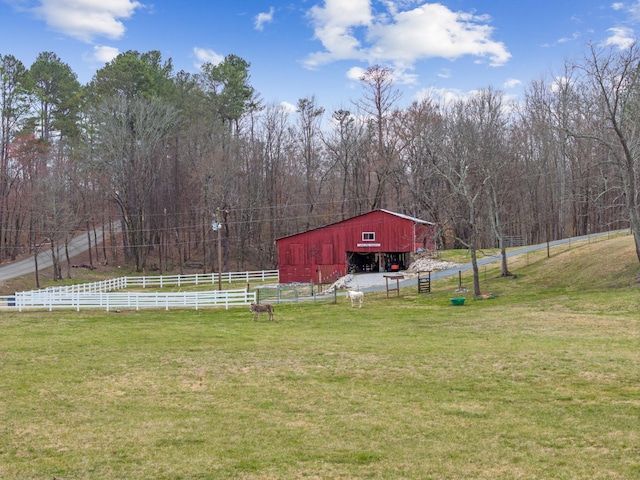 view of yard featuring a barn, fence, a rural view, an outdoor structure, and a wooded view