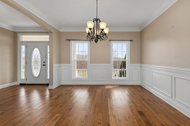 entrance foyer featuring wainscoting, an inviting chandelier, ornamental molding, and dark wood-type flooring