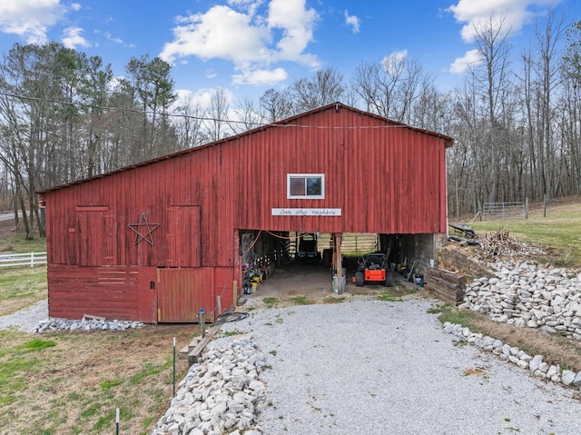 view of outdoor structure with gravel driveway, fence, and an outbuilding