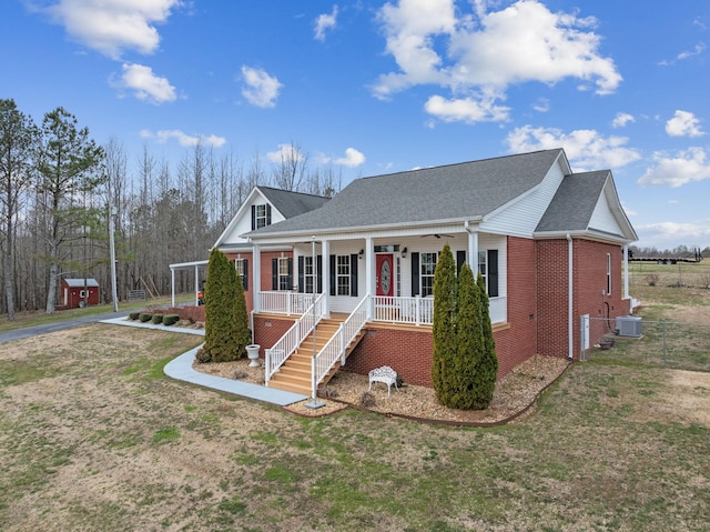 view of front facade with central AC unit, a porch, a front yard, brick siding, and roof with shingles