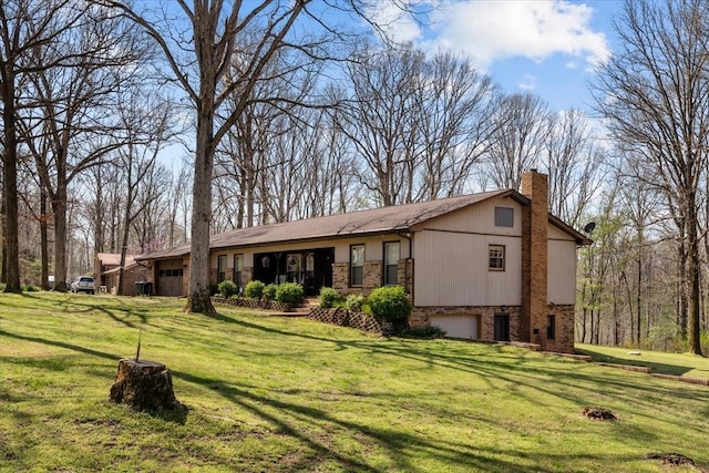 back of house featuring a garage, a yard, brick siding, and a chimney