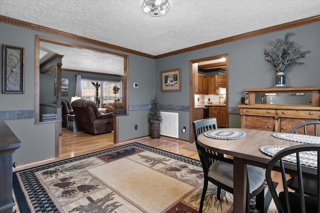dining area with light wood-style flooring, visible vents, a textured ceiling, and ornamental molding