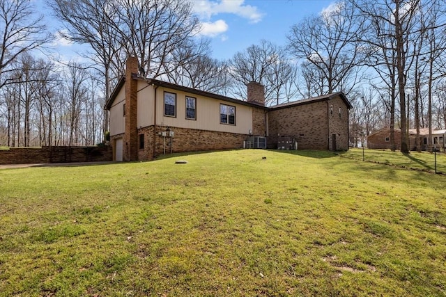 back of house featuring a chimney, an attached garage, brick siding, and a yard