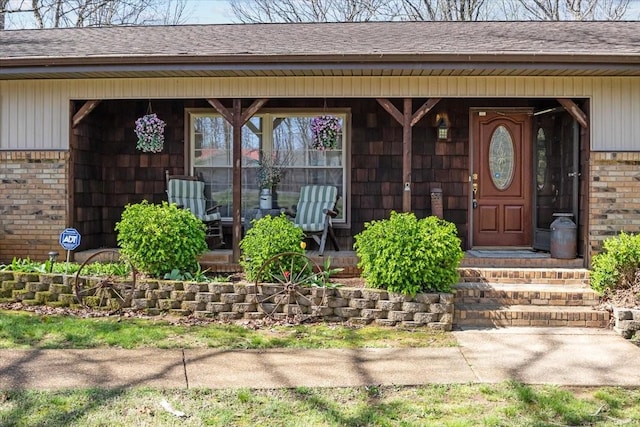 property entrance with covered porch, brick siding, and roof with shingles