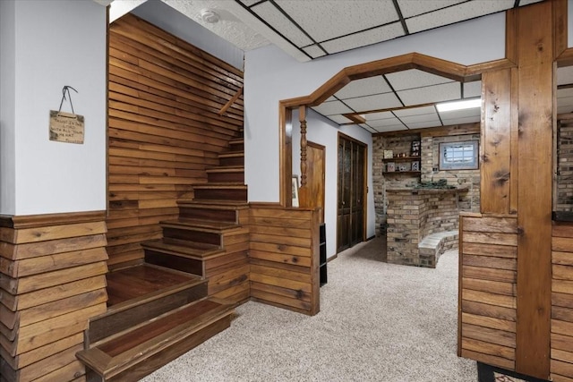 stairs featuring a wainscoted wall, wood walls, carpet flooring, and a paneled ceiling