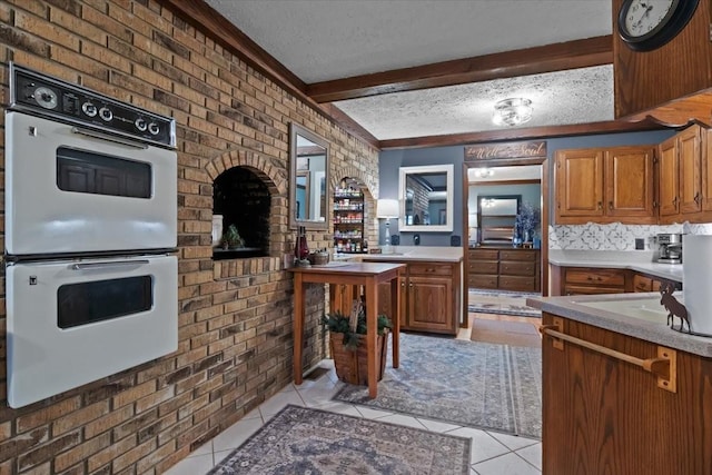 kitchen featuring light countertops, light tile patterned flooring, beam ceiling, and double oven