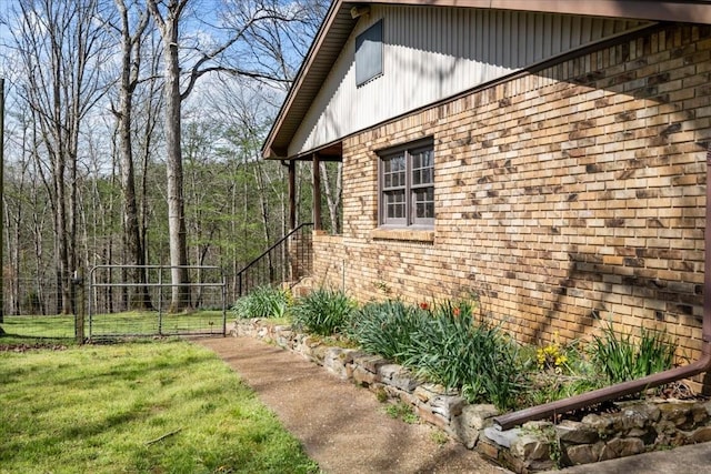 view of home's exterior featuring fence, a lawn, brick siding, and a gate