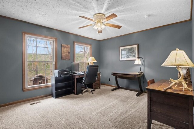 carpeted home office featuring a textured ceiling, visible vents, baseboards, a ceiling fan, and ornamental molding