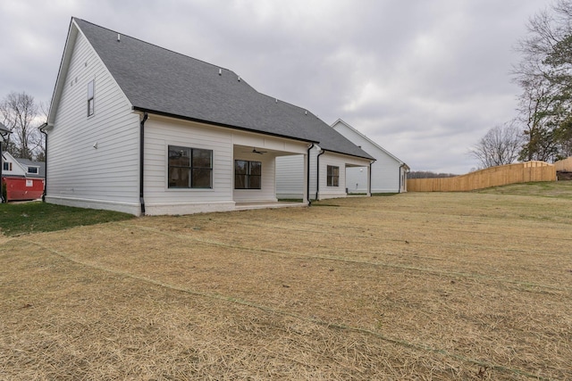 rear view of house featuring fence, ceiling fan, a shingled roof, and a yard