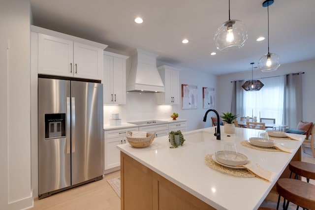 kitchen with custom exhaust hood, a sink, black electric cooktop, a kitchen bar, and stainless steel refrigerator with ice dispenser
