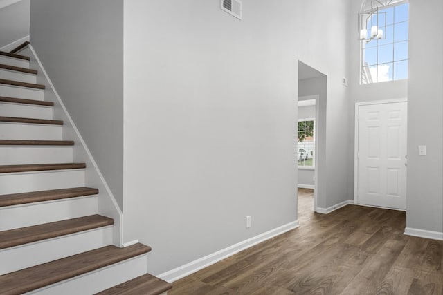 foyer with stairway, wood finished floors, a chandelier, baseboards, and a high ceiling
