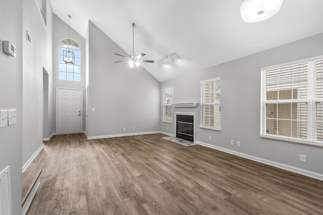 unfurnished living room with wood finished floors, a ceiling fan, a fireplace with flush hearth, baseboards, and high vaulted ceiling